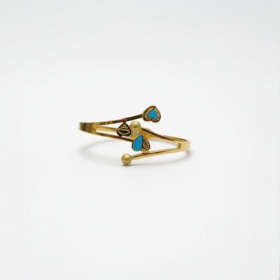 A close-up of an elegant gold cuff bracelet featuring three small turquoise heart-shaped accents and two gold spherical beads, set against a clean white background.