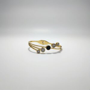 A stylish gold-toned bangle bracelet featuring a central black circular enamel detail surrounded by sparkling cubic zirconia paved circles, presented on a white background.