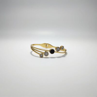 A stylish gold-toned bangle bracelet featuring a central black circular enamel detail surrounded by sparkling cubic zirconia paved circles, presented on a white background.