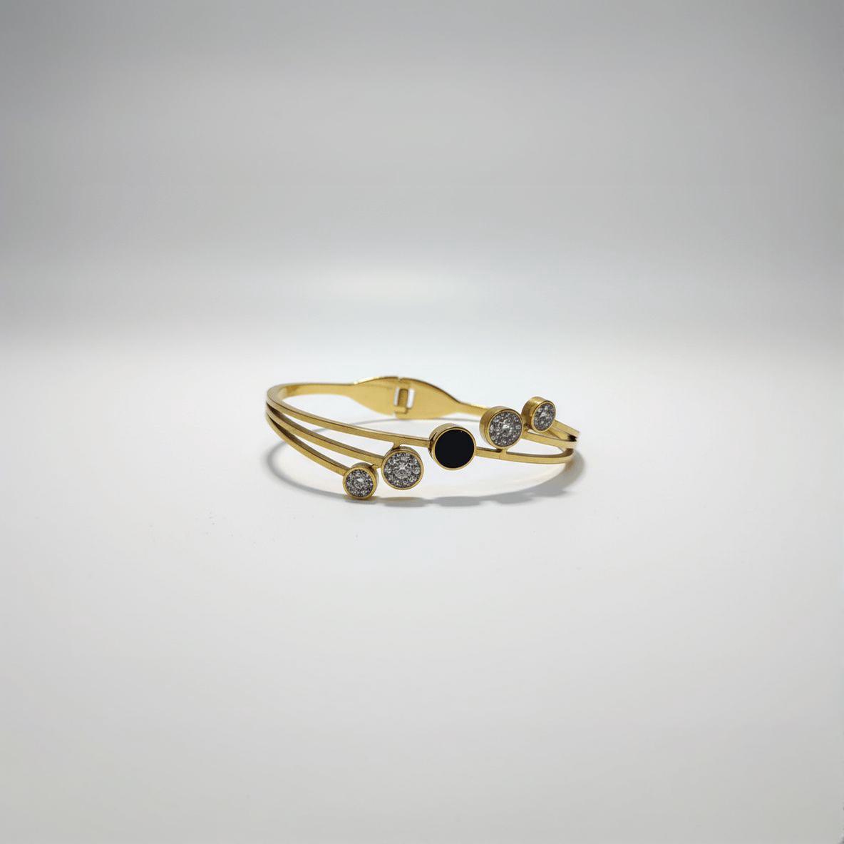 A stylish gold-toned bangle bracelet featuring a central black circular enamel detail surrounded by sparkling cubic zirconia paved circles, presented on a white background.